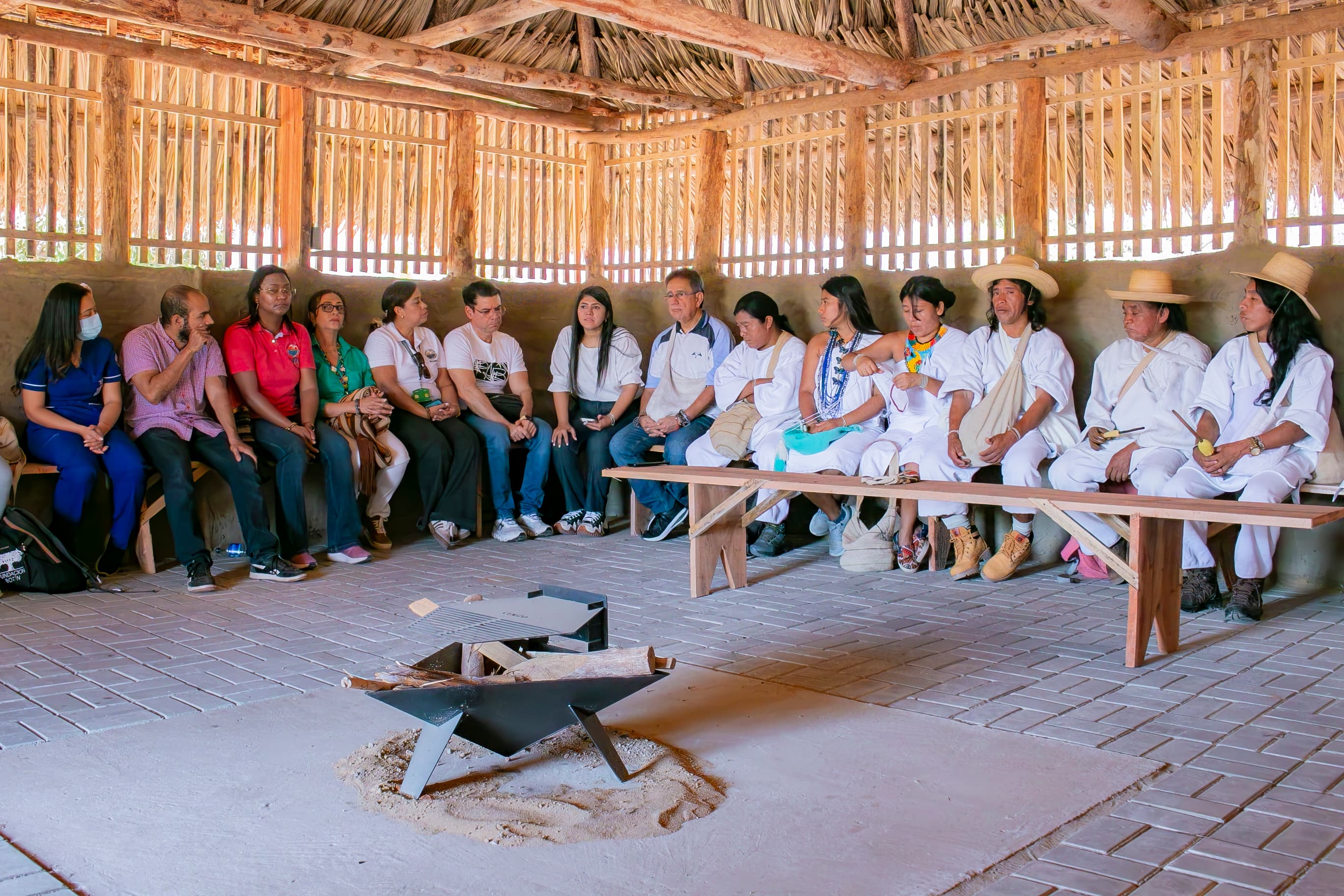 Autoridades tradicionales, docentes y estudiantes reunidos en círculo alrededor del fogón, en el interior de la Kankʉrwa